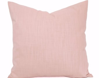 May include: A soft, blush pink throw pillow with a subtle textured fabric.