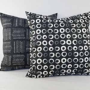 May include: Two square throw cushions featuring black and white fabric. The front cushion displays a repeating pattern of white hand-drawn circles on a black background, while the back cushion features a pattern of white dashed lines in blocks.