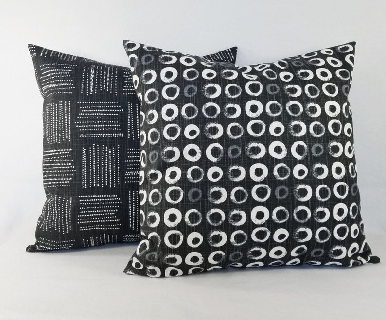 May include: Two square throw cushions featuring black and white fabric. The front cushion displays a repeating pattern of white hand-drawn circles on a black background, while the back cushion features a pattern of white dashed lines in blocks.