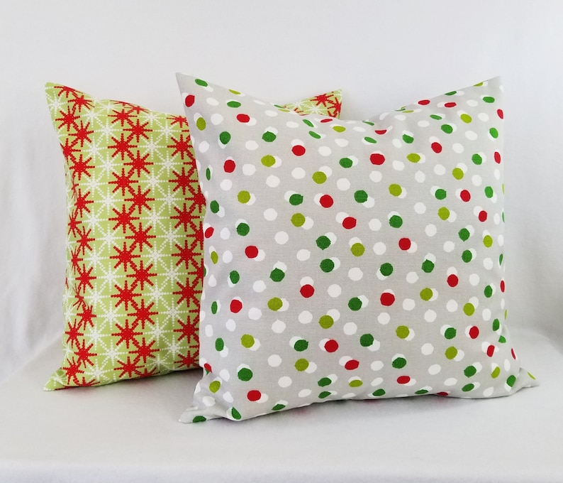 May include: Two decorative throw pillows with a Christmas theme. One pillow has a green and red snowflake pattern, and the other has a gray background with red and green polka dots.
