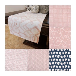 May include: A white and blush pink geometric patterned table runner draped over a dark wooden table. The image also shows close-ups of various fabric patterns in pink and navy blue, including geometric, dotted, and textured designs.