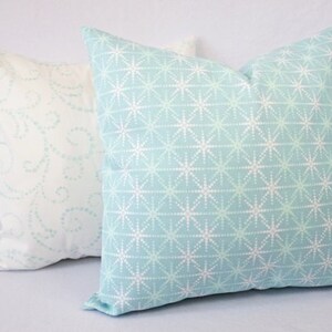 May include: Two decorative throw pillows, one with a white background and a light blue swirl pattern, and the other with a light blue background and a white starburst pattern.