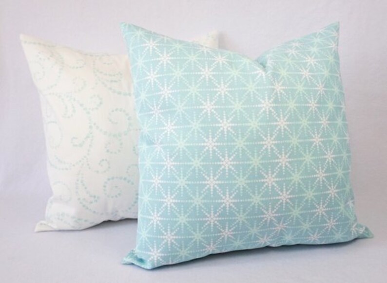 May include: Two decorative throw pillows, one with a white background and a light blue swirl pattern, and the other with a light blue background and a white starburst pattern.