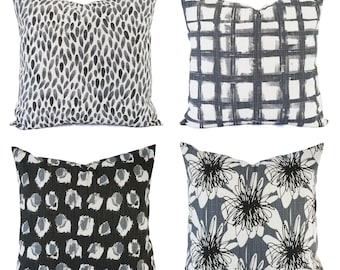 May include: A set of four square throw pillows featuring distinct black and white patterns. The designs include a black teardrop print, a black grid pattern, a black and gray spotted print, and a black and white floral line art design.