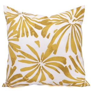May include: Square white throw pillow with a gold floral pattern. The design features large, stylized flowers in a golden hue against a white background. The pillow is a decorative accent for a sofa or bed.