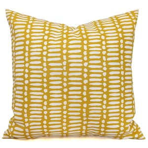 May include: Square decorative pillow with a mustard yellow background and a repeating pattern of white dashes. The pillow has a soft, textured appearance and is likely made of fabric. The design is modern and would complement various home decor styles.