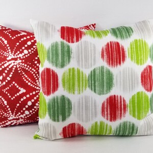 May include: Two square throw pillows. The front pillow features a white background with a repeating pattern of red, lime green, and light gray circles. The back pillow is red with a white dotted geometric pattern arranged in a diamond motif.