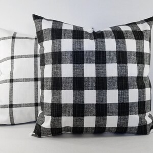 May include: Two square throw cushions featuring a black and white pattern. The front cushion displays a dense black and white buffalo check pattern, while the cushion positioned behind it features a larger, sparse black and white grid pattern.