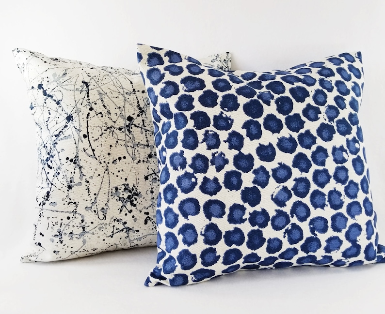 Puede incluir: Dos almohadas decorativas con fondo blanco y patrones azules. Una almohada tiene un dise&ntilde;o de pintura salpicada, mientras que la otra tiene un patr&oacute;n de lunares azules y blancos.