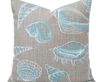 May include: A gray throw pillow with a blue and white seashell pattern. The pillow is made of a textured fabric and has a square shape.