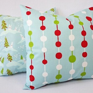 May include: Two decorative throw pillows with a blue background. One pillow has a pattern of red, white, and green circles. The other pillow has a pattern of white rabbits and green trees on a blue background.