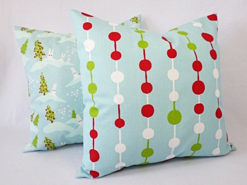 May include: Two decorative throw pillows with a blue background. One pillow has a pattern of red, white, and green circles. The other pillow has a pattern of white rabbits and green trees on a blue background.