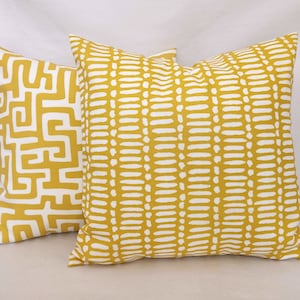 May include: Two decorative throw pillows with mustard yellow fabric and white patterns. One pillow features a maze-like design, while the other has a dotted pattern. The pillows are square and appear to be made of a soft fabric.