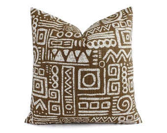 May include: A square throw pillow featuring a brown fabric base with a white, distressed-style geometric pattern. The design consists of various shapes including circles, squares, triangles, and zig-zag lines arranged in a repeating, block-like layout.