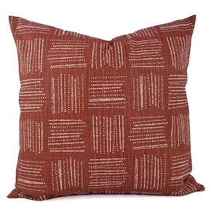 May include: A rust-colored throw pillow with a white geometric pattern. The pattern is made up of small white dots arranged in lines and squares.