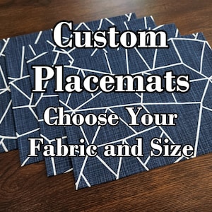 May include: Three blue and white geometric patterned placemats stacked on a wooden surface. The text "Custom Placemats Choose Your Fabric and Size" is superimposed on the image.