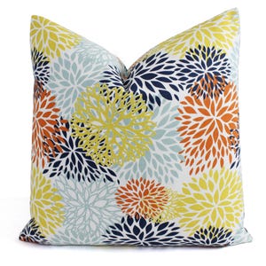 Puede incluir: Una almohada decorativa con un patrón floral en tonos amarillos, naranjas, azules y blancos. La almohada presenta una impresión a gran escala de flores estilizadas.