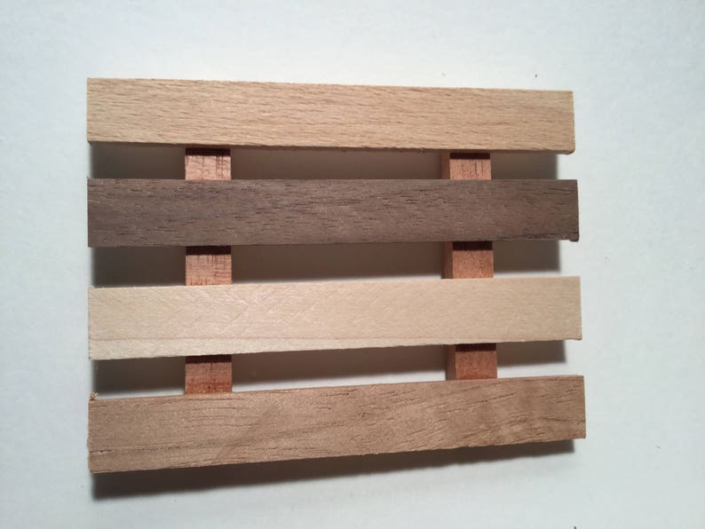 May include: A wooden soap dish with four slats, each a different shade of wood. The top slat is light brown, the second is dark brown, the third is light beige, and the bottom slat is a medium brown.