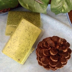 May include: Two bars of green and yellow soap on a blue towel with a brown pine cone.