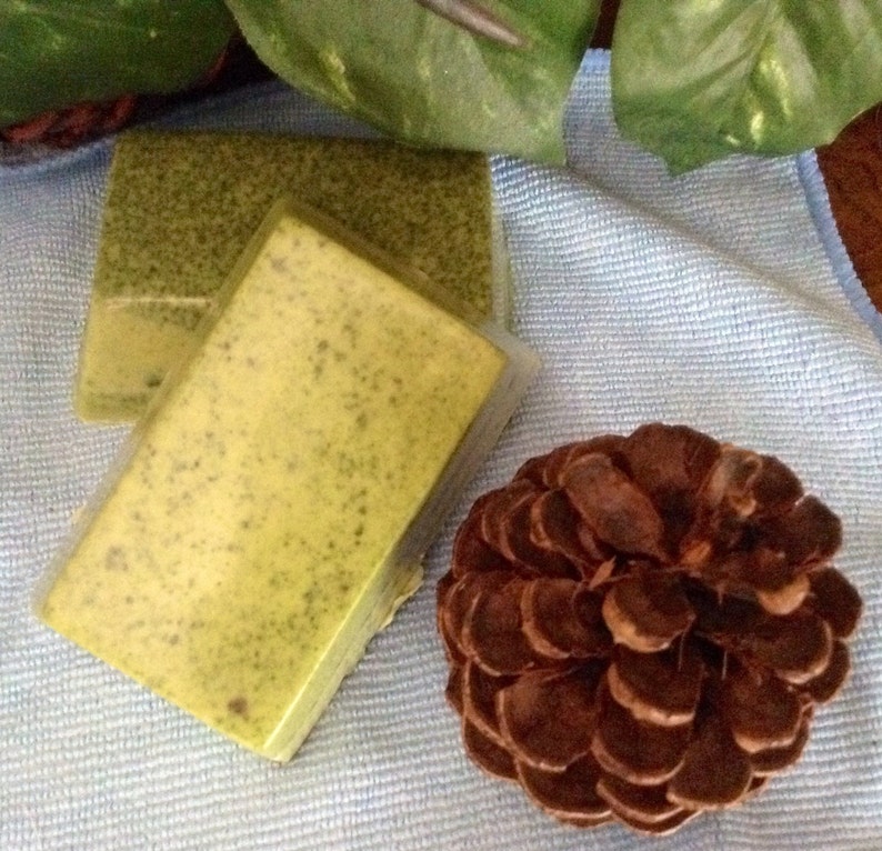 May include: Two bars of green and yellow soap on a blue towel with a brown pine cone.