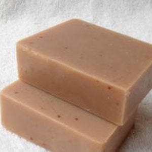 Könnte beinhalten: Zwei handgemachte Seifenstücke, eines auf dem anderen. Die Seife ist hellbraun mit kleinen roten Flecken.
