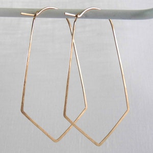 May include: A pair of gold-toned geometric hoop earrings. The earrings are made of thin wire and have a slightly irregular shape.