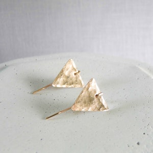 May include: A pair of gold triangle earrings with a hammered texture. The earrings are simple and modern, and would make a great gift for any occasion.