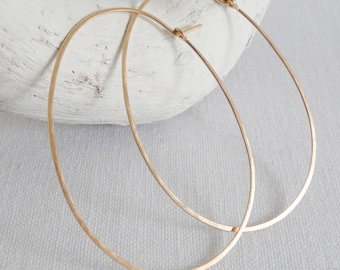 May include: A pair of large, gold-toned hoop earrings. The hoops are thin and have a slightly oval shape.