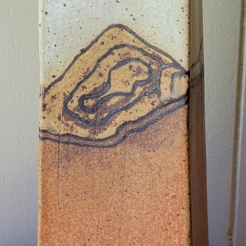 May include: A rectangular ceramic vase with a textured surface. The top portion is off-white with a brown, layered design. The bottom half is a reddish-brown color. The vase has a rustic, handmade appearance.