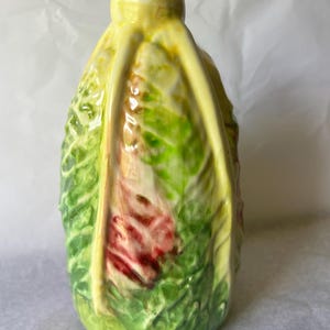 May include: A ceramic vase shaped like a head of lettuce with a narrow neck opening. The surface features a textured, leafy design in shades of vibrant green, pale yellow, and deep red, with prominent raised veins running vertically along the exterior.