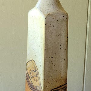 May include: Tall, rectangular ceramic vase with a speckled off-white upper section and a textured, brown lower section. The vase has a narrow neck and a flared top. Decorative pottery.