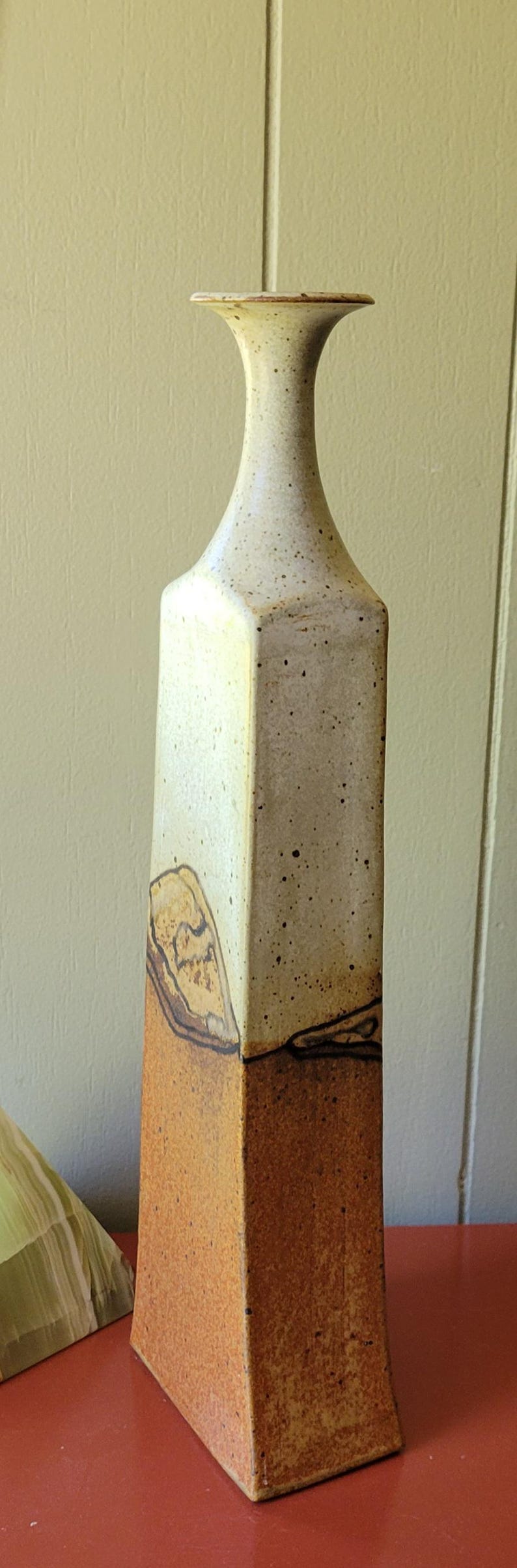 May include: Tall, rectangular ceramic vase with a speckled off-white upper section and a textured, brown lower section. The vase has a narrow neck and a flared top. Decorative pottery.