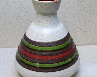 May include: A ceramic vase with a speckled white body and a dark red interior. The vase features horizontal bands of brown, green, and red around its lower half. The vase has a bulbous base and a narrow neck.