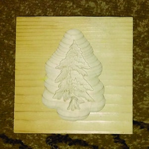 May include: A wooden Christmas cookie cutter in the shape of a pine tree. The cutter is made of light wood and has a detailed design.