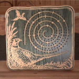 May include: A wooden game board with a spiral pattern and a pheasant design. The board is painted green and has a light brown pheasant with a long tail.
