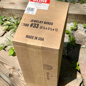 May include: A rectangular cardboard box labeled "JEWELRY BOXES" with the text "100 #33 (3 1/2 x 3 1/2 x 1)". The box has a red and white label that says "ULINE". The box is made in the USA.