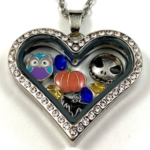 May include: Silver heart-shaped locket necklace with a clear glass insert. The locket contains a variety of charms, including a purple owl, a pumpkin, a Jack Skellington character, and a ghost.