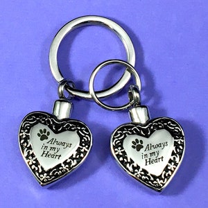 May include: Silver keychain with two heart-shaped cremation urns. Each urn has a paw print and the inscription "Always in my Heart".