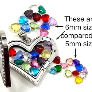 May include: A silver heart-shaped locket with a hinged opening, filled with colorful heart-shaped gems. The gems are in various colors, including red, blue, green, and yellow. Text indicates the gems are 6mm and 5mm in size.