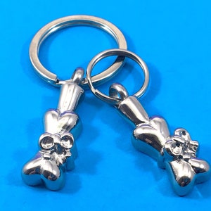 May include: Two silver keychains with a bone-shaped charm. Each charm has a heart-shaped design with a bow at the top.