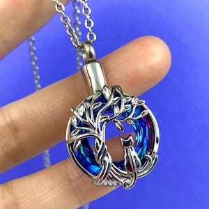 May include: Silver necklace with a blue and purple iridescent glass pendant featuring a tree of life design with a cat sitting in the branches.