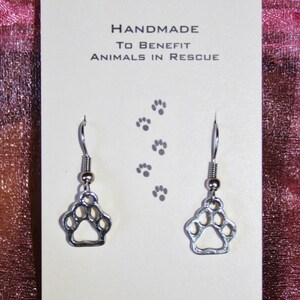 May include: Silver paw print dangle earrings on a white card with the text "RescueArtWorks! Handmade to benefit animals in rescue" and the email address "rescuemeva@yahoo.com".