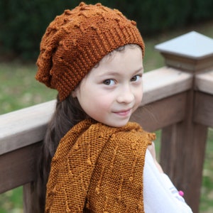May include: A young person wearing a brown knitted hat and matching scarf. The scarf has a textured pattern and the hat is slouchy.