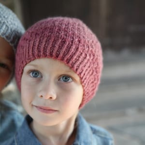 May include: A young person wearing a pink knitted hat and a blue denim jacket. The person is looking at the camera.