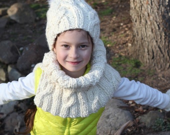 May include: A young person wearing a white knitted hat with a pom-pom, a white knitted scarf, a yellow puffer vest, and white pants.