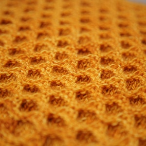 May include: A close-up of a waffle weave fabric in a warm yellow color. The fabric has a textured, waffle-like pattern.