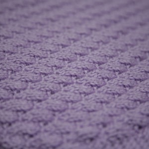 May include: A close-up of a soft, purple knitted fabric with a textured pattern.