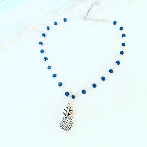 May include: A silver pineapple charm hangs from a delicate silver chain with dark blue beads.