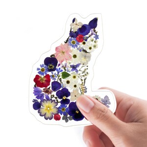 May include: A sticker of a cat silhouette made of pressed flowers. The flowers are in shades of blue, purple, pink, red, and white.