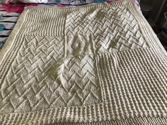 Cream colored acrylic baby blanket in geometric patterns with a Diamond pattern in the middle.